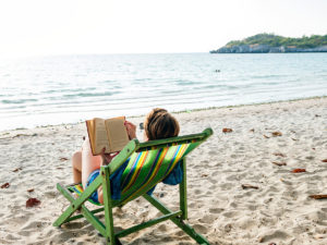 Mulher lê livro sentada em cadeira na praia